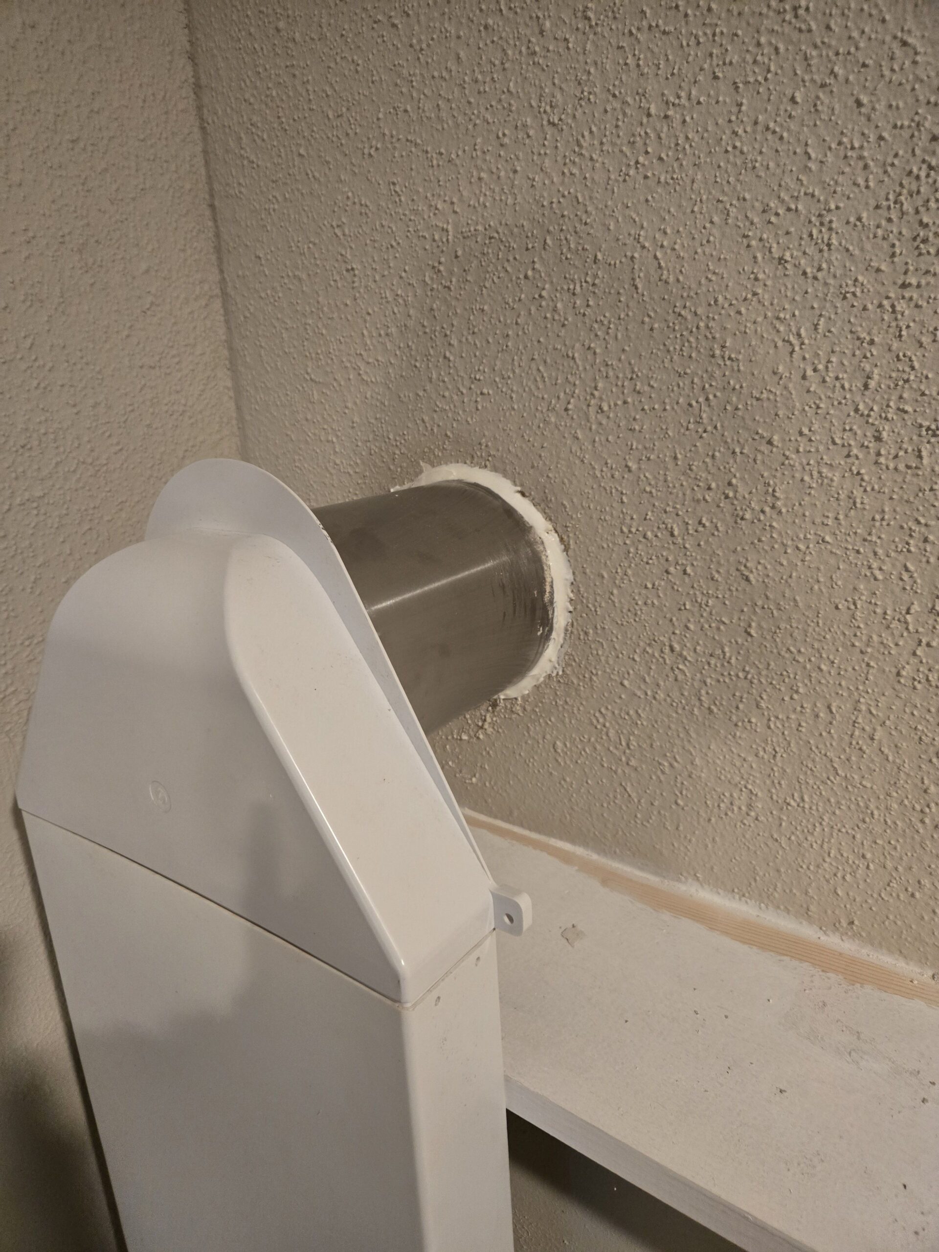 EZ Breathe is installed on a textured beige wall, with a metal duct extending through an opening.