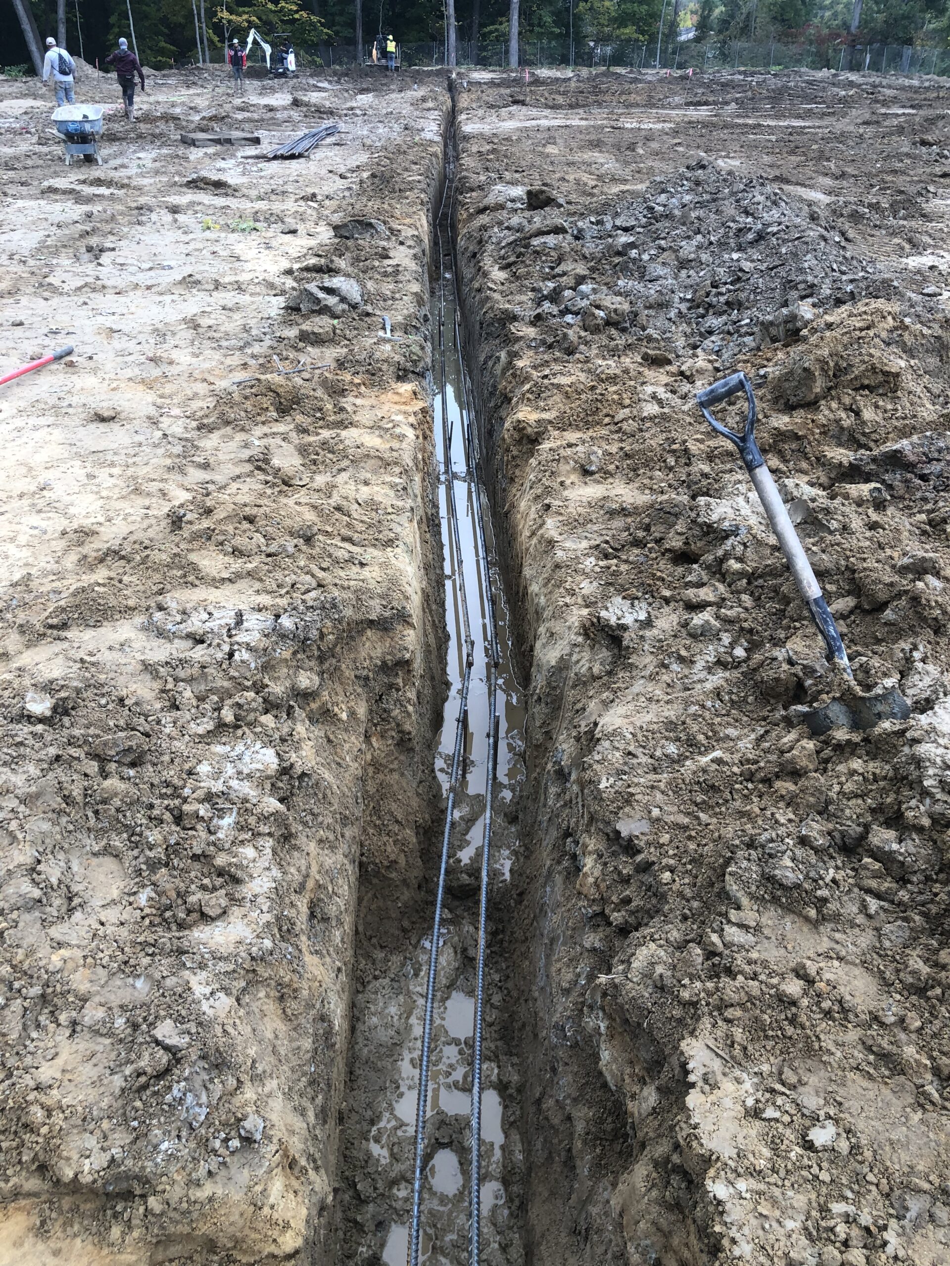 A long, narrow trench with pipes running through it, partially filled with water in Beecher IL